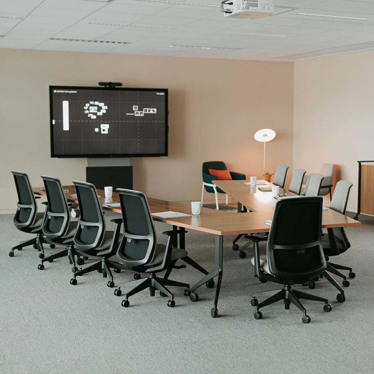 A large v-shaped table with lots of office chairs facing a monitor on the wall